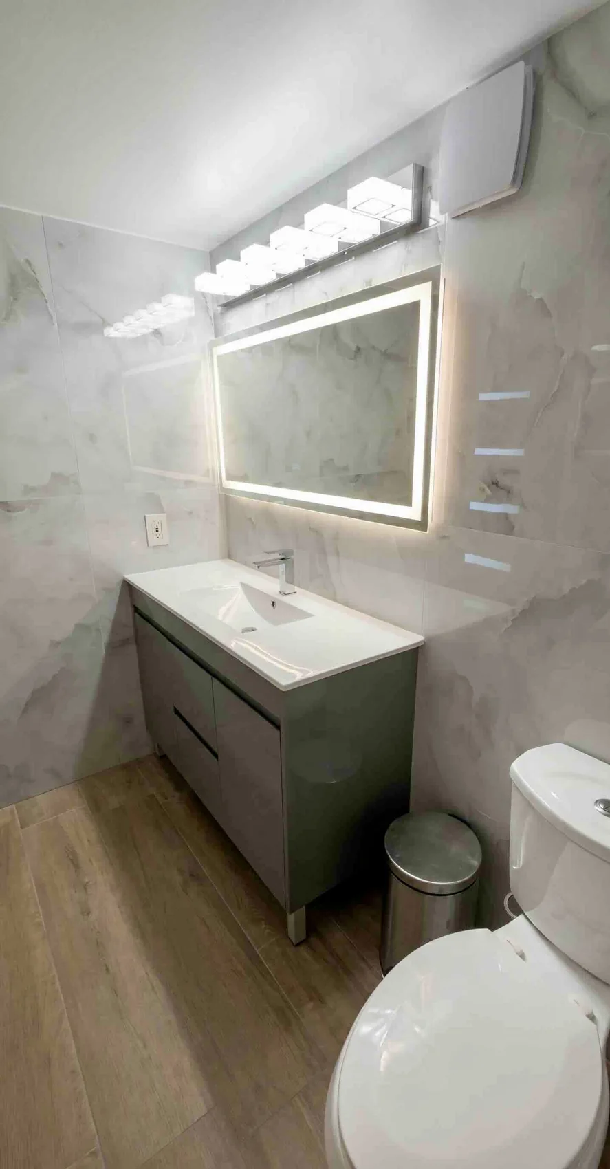 Light wall tile, wood-look flooring and a compact vanity in a coordinated bathroom.