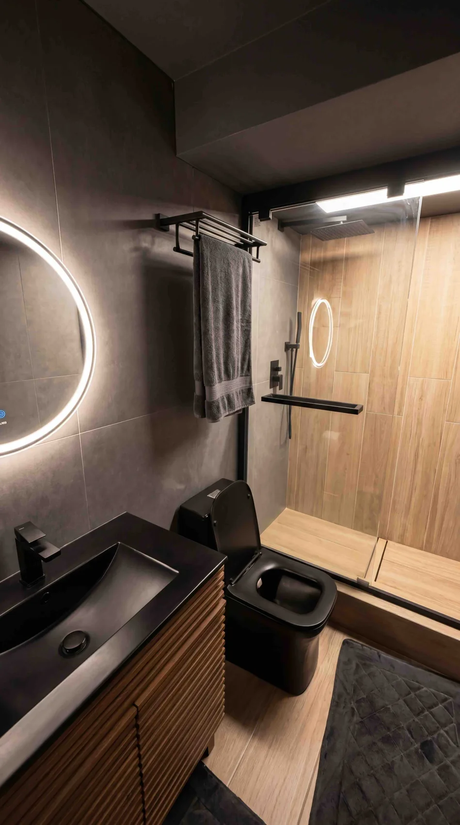 Dark bathroom with wood vanity and illuminated round mirror