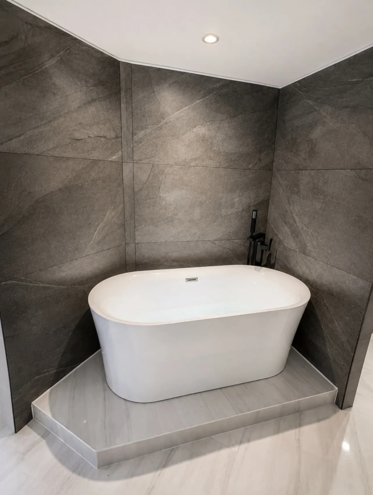 A freestanding white bathtub framed by dark stone-look surfaces.